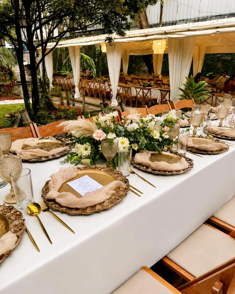 Pabellón con cortinas de gasa, mesa larga con flores y sillas de madera a la luz del día