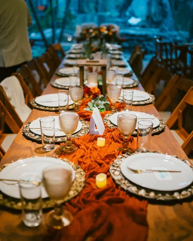 Mesa con runner terracota, copas labradas y velas al caer la tarde