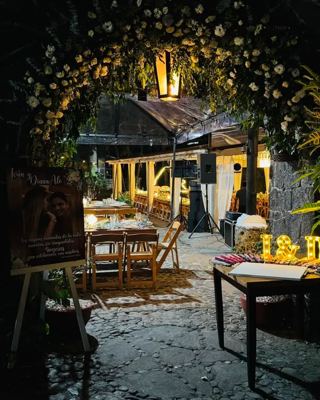 El arco de piedra de la entrada cubierto de flores blancas, con el farol encendido de noche